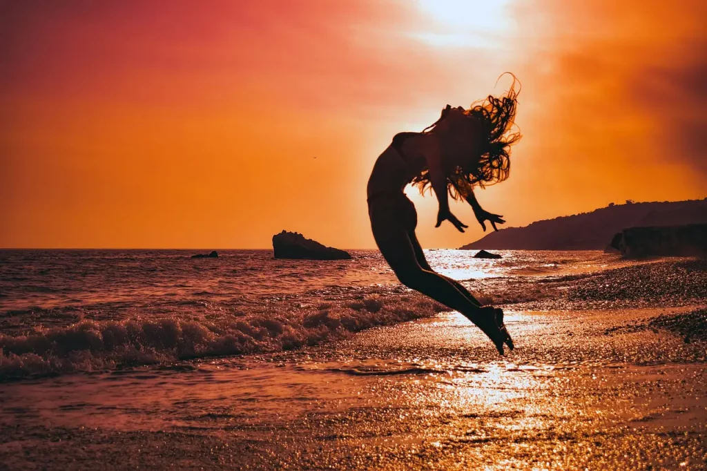 Sur cette photo, une femme exulte au bord de la plage au coucher du soleil, symbolisant sa joie de liberté et de victoire sur les obstacles de la vie. Une véritable illustration de la réussite et de l'accomplissement des objectifs.
