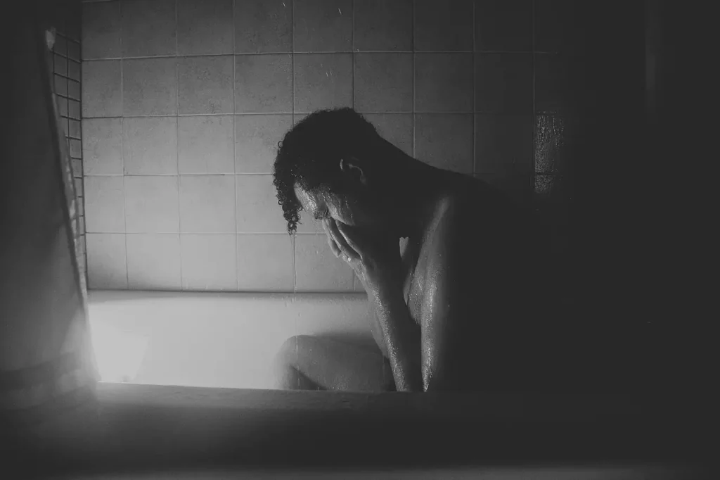 Cette image en noir et blanc capture la détresse émotionnelle d'un homme, recroquevillé dans sa baignoire, les larmes coulant sur son visage. C'est une représentation poignante des luttes intérieures associées au schéma d'échec, mettant en lumière la douleur et la vulnérabilité ressenties face à ce sentiment persistant.