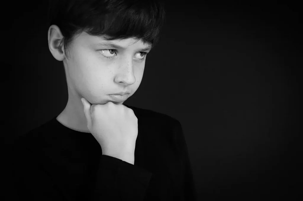 Dans un monde teinté de gris, l'enfant de l'innocence se tient, son regard empreint de colère et de bouderie. Son poing serré sous son menton, il exprime le poids du schéma de méfiance et d'abus, portant le fardeau des traumatismes invisibles. Dans son regard, une lueur de défi mêlée de tristesse, une toile complexe de douleur et de désespoir. Trop jeune pour comprendre, trop seul pour combattre, il porte le poids d'un fardeau qui n'est pas le sien.
