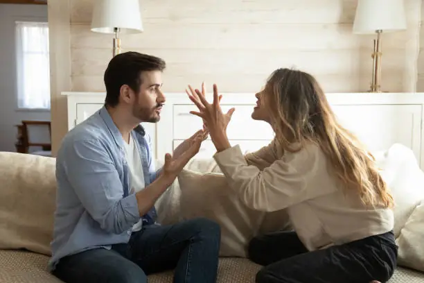 Sur cette image, un couple est assis sur un canapé, mais l'atmosphère est tendue et chargée d'émotions négatives. Leur langage corporel et leurs expressions faciales révèlent une dispute intense, illustrant les conflits et les tensions souvent associés aux relations amoureuses marquées par le schéma d'imperfection.