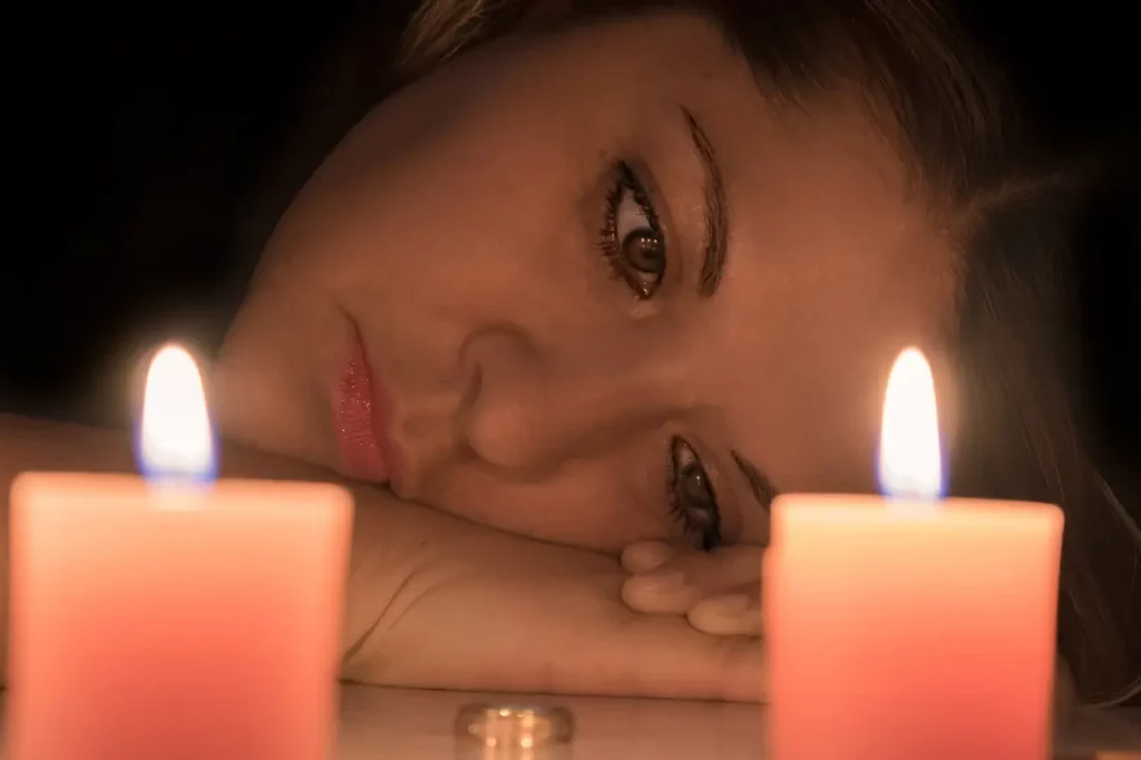 Dans cette image émouvante, une femme est capturée dans un moment de profonde tristesse, sa tête reposant dans ses mains, une alliance abandonnée devant elle. Les deux bougies allumées au premier plan ajoutent une ambiance de recueillement. Cette scène semble évoquer le tumulte émotionnel d'une séparation récente, mettant en lumière le sentiment d'abandon et de désespoir. Une représentation saisissante de la douleur et de la solitude ressenties dans les moments de rupture.