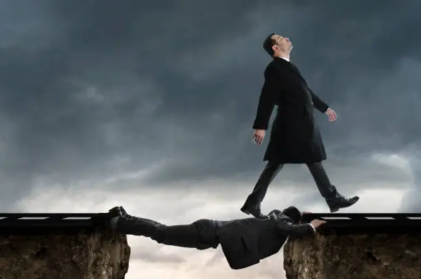 Découvrez les signaux de danger dans les relations amoureuses liés au schéma «tout nous est dû» à travers cette image saisissante. Sur un fond de ciel nuageux, deux falaises symbolisent les obstacles dans une relation. Un homme, revêtu de noir, se trouve allongé entre ces falaises, faisant office de pont pour faciliter le passage. Pendant ce temps, un autre homme, également vêtu de noir, le franchit avec une expression hautaine et le nez en l'air, illustrant ainsi une dynamique de domination et de manque d'empathie. Explorez les subtilités de ces schémas comportementaux et apprenez à reconnaître les signes avant-coureurs de relations potentiellement toxiques pour cultiver des liens plus sains et équilibrés.